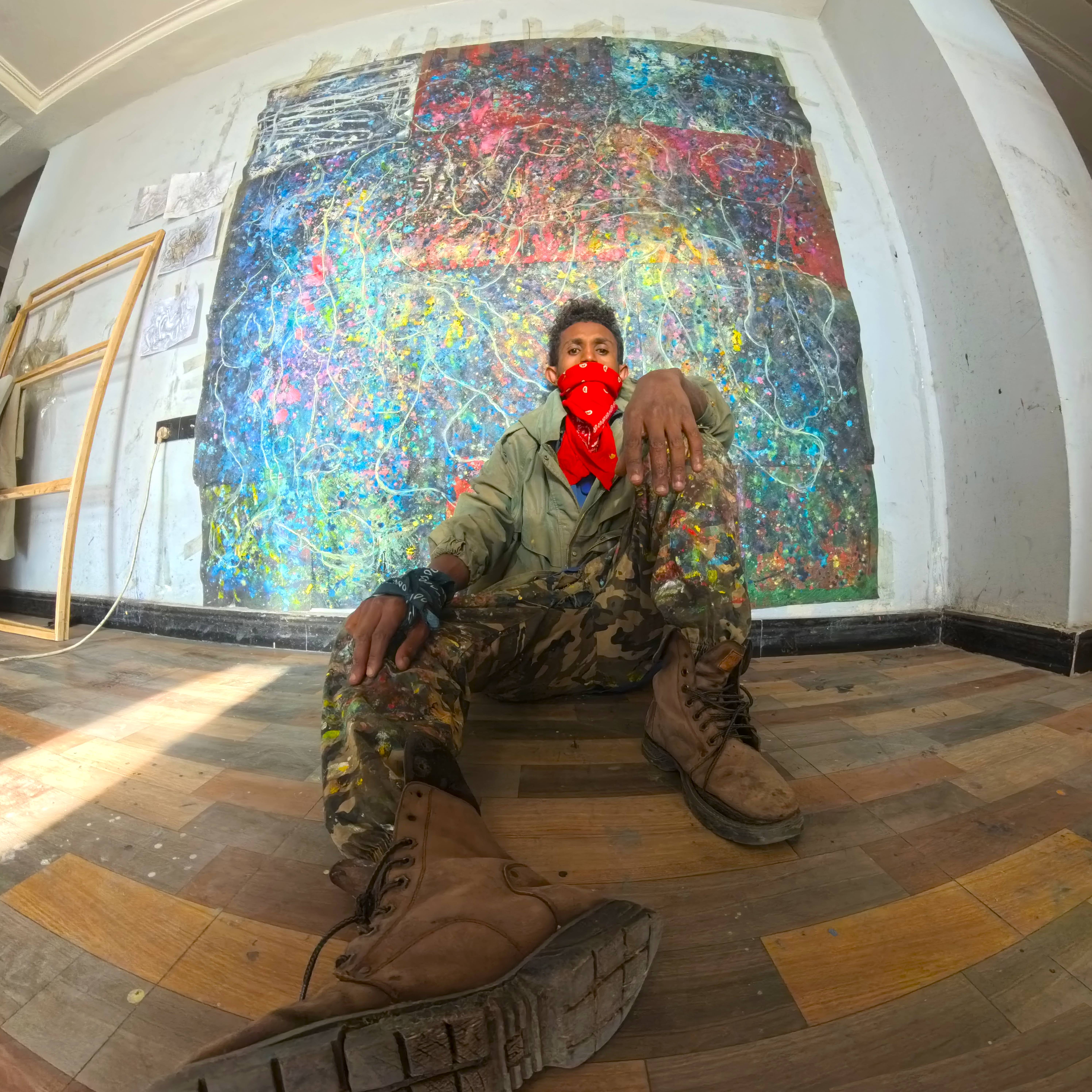 Birhanu Daniel seated in his studio in front of a colourful painting